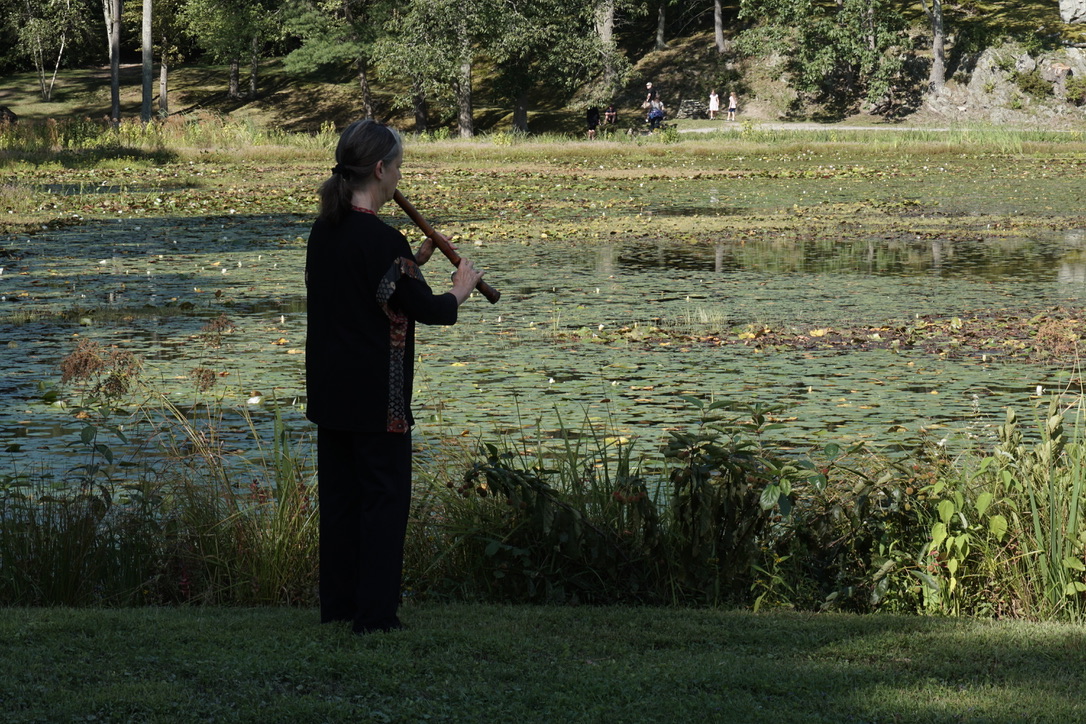 Elizabeth Brown playing shakuhachi next to a lake.